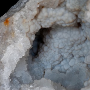 May include: A close-up of a geode with a white exterior and a blue interior. The interior of the geode is filled with small, round crystals.