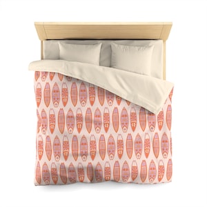 May include: A bed with a light wood headboard, two white pillows, and a cream-coloured duvet cover. The duvet features a repeating pattern of orange and purple surfboards on a light pink background. The surfboards have intricate floral designs.