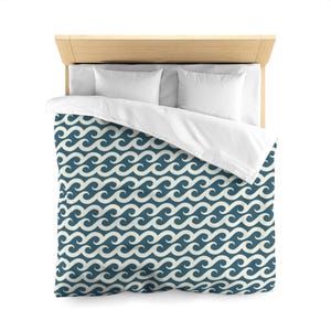 May include: A bed with a light wood headboard, white pillows, and a white duvet cover. The duvet cover features a repeating wave pattern in teal and off-white, creating a nautical theme. The bed is neatly made, suggesting a focus on home decor.