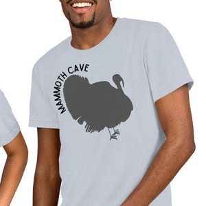 May include: Two people wearing light blue t-shirts with a silhouette of a turkey and the text "Mammoth Cave" printed on the front.