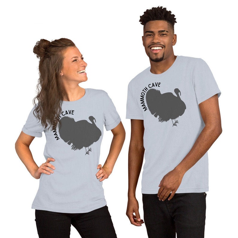 May include: Two people wearing light blue t-shirts with a silhouette of a turkey and the text "Mammoth Cave" printed on the front.