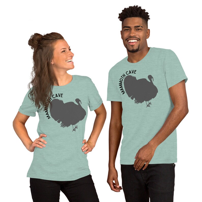May include: Two people wearing light blue t-shirts with a gray turkey silhouette and the text "Mammoth Cave" printed on the front.
