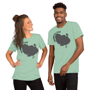 May include: Two people wearing light green t-shirts with a silhouette of a turkey and the text "Mammoth Cave" printed on the front.
