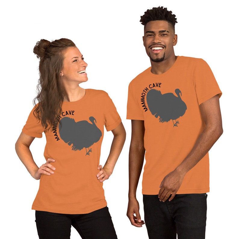 May include: Two people wearing orange short-sleeved t-shirts with a gray turkey silhouette and the text "Mammoth Cave" printed on the front.