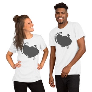May include: Two people wearing white t-shirts with a gray turkey silhouette and the text "Mammoth Cave" printed on the front.