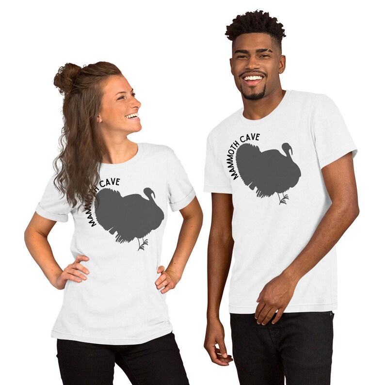 May include: Two people wearing white t-shirts with a gray turkey silhouette and the text "Mammoth Cave" printed on the front.