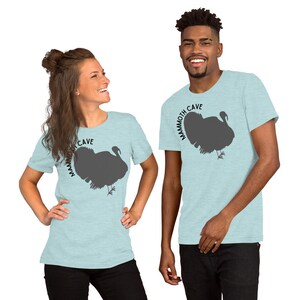 May include: Two people wearing light blue t-shirts with a gray silhouette of a turkey and the text "Mammoth Cave" printed on the front.