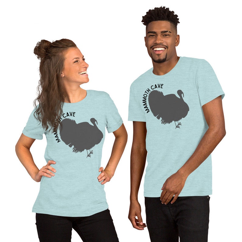 May include: Two people wearing light blue t-shirts with a gray silhouette of a turkey and the text "Mammoth Cave" printed on the front.