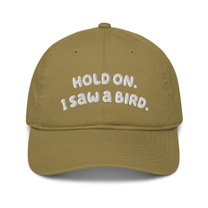 May include: A khaki green baseball cap with white embroidered text that reads "Hold on. I saw a bird."