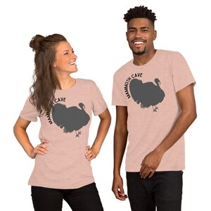 May include: Two people wearing pink heather t-shirts with a silhouette of a turkey and the text "Mammoth Cave" printed on the front.