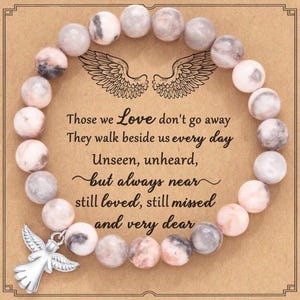 May include: A beaded bracelet with light pink and gray stone beads. The bracelet is on a card with the text "Those we Love don't go away..." and a silver angel charm.