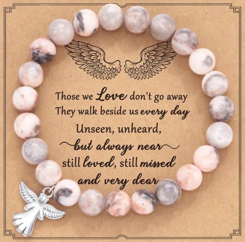 May include: A beaded bracelet with light pink and gray stone beads. The bracelet is on a card with the text "Those we Love don't go away..." and a silver angel charm.