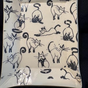 May include: A rectangular ceramic tray with a cream-colored base featuring a repeating pattern of black line-drawn cats in various poses, including stretching, sitting, and walking, with long curled tails and detailed whiskers.