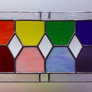 May include: A rectangular stained glass panel with a rainbow color scheme. The panel features red, yellow, green, and blue squares, with white diamond shapes and a silver metal frame. Includes hanging hooks.