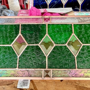 May include: A rectangular stained glass panel with a copper-colored frame. The panel features textured green glass sections, diamond-shaped accents, and iridescent glass borders. The design is symmetrical and detailed, showcasing various colors and textures.