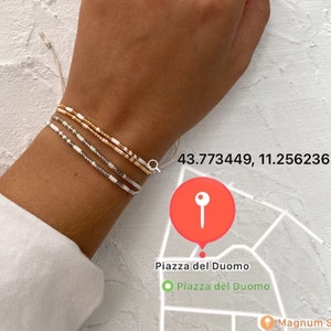 Könnte beinhalten: Ein Set aus drei Perlenarmbändern an einem Handgelenk. Die Armbänder sind aus weißen, goldenen und silbernen Perlen gefertigt. Die Armbänder sind übereinander gestapelt.