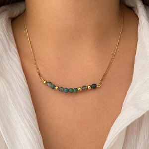 May include: A gold-toned chain necklace featuring a central horizontal arrangement of small, round, mottled green beads interspersed with smooth, polished gold-toned spherical beads, creating a delicate and balanced decorative focal point.