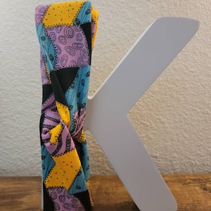 May include: A black, blue, yellow, and purple patterned headband with a knotted design. The headband is made of fabric and has a patchwork design.