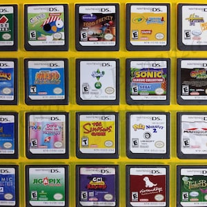 May include: A collection of 18 Nintendo DS game cartridges displayed in a yellow plastic case. The cartridges are arranged in three rows of six. The games include titles such as "Club House Games", "Go Petz", "Food Frenzy", "Madagascar 3", "Naruto Ninja Destiny", "The Sims 3", "Sonic Classic Collection", "Quest 64", "Tinker Bell", "Dora Saves the Mermaids", "The Simpsons Game", "Petz Nursery 2", "Mario Kart DS", "Cosmic Destruction", "Jigapix", "CN Racing", "Nintendogs", and "Tinker Bell".