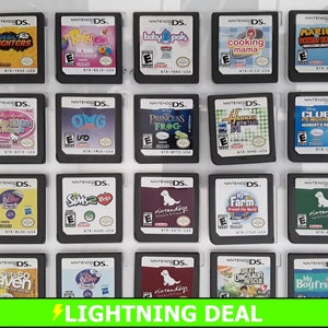 May include: A collection of 20 Nintendo DS game cartridges, displayed in a clear plastic case. The cartridges are arranged in four rows of five, with each cartridge featuring a different game title and cover art. The games include titles such as "Fossil Fighters", "My Baby Girl", "Baby Pals", "Cooking Mama", "Mario & Sonic at the Olympic Games", "Hello Kitty & Friends", "OMG", "Princess Frog", "Hannah Montana", "Club Penguin", "My Scene Friends", "Sims 2 Pets", "Nintendogs", "My Farm", "Nintendogs", "That's So Raven", "The Suite Life of Zack & Cody", "Nintendogs", "Great Dinosaur Rescue", and "My Boyfriend".