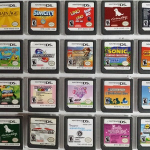 May include: A collection of 18 Nintendo DS game cartridges, displayed in a clear plastic case. The cartridges are arranged in three rows of six, with each cartridge featuring a different game title and cover art. Some of the games include Brain Age, SimCity DS, Uno Skip-Bo, Nintendogs, Dawn of a New Life, Magnetica, and Sonic Classic Collection.