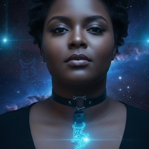 Puede incluir: Una persona con un collar negro con diseño de orejas de gato y un colgante azul brillante. El colgante presenta una figura estilizada. El fondo es una escena espacial azul oscuro con estrellas y nebulosas.