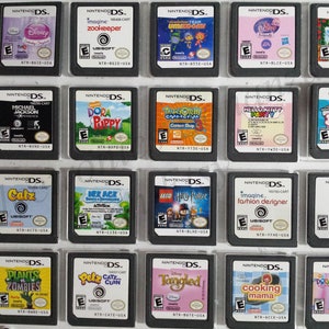 Puede incluir: Una colección de 20 cartuchos de juego de Nintendo DS, expuestos en una caja de plástico transparente. Los cartuchos están dispuestos en cuatro filas de cinco, con cada cartucho presentando un título de juego y una ilustración de portada diferentes. Algunos de los juegos incluyen "Plants vs. Zombies", "Catz", "Dora la Exploradora", "Imagine: Fashion Designer" y "Cooking Mama".
