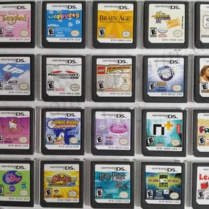 Może przedstawiać: Kolekcja 20 gier na Nintendo DS w przezroczystym plastikowym pudełku. Gry są ułożone w cztery rzędy po pięć. Gry są w różnych kolorach i mają różne tytuły. Niektóre z tytułów to "Tangled", "Wappy Dog", "Brain Age", "Hannah Montana: Music Jam", "100 Classic Books", "Up", "Mario Kart DS", "Lego Indiana Jones", "Minute to Win It", "Lillian Fitness Ultimate 2010", "Hello Kitty", "Sonic Rush Adventure", "Disney Princess", "n+", "Pac-Pix", "Littlest Pet Shop", "Kirby Super Star Ultra", "Harry Potter", "Ben 10: Vilgax Attacks" i "Learn Math".