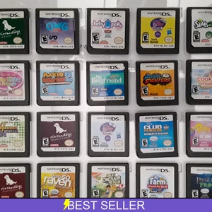Puede incluir: Una colección de 20 cartuchos de juegos de Nintendo DS, expuestos en una caja de plástico transparente. Los cartuchos presentan una variedad de juegos populares, incluyendo "nintendogs", "Cooking Mama", "My Boyfriend", "Fossil Fighters", "Hannah Montana", "Club Penguin", "Princess Frog", y "There So Raven".