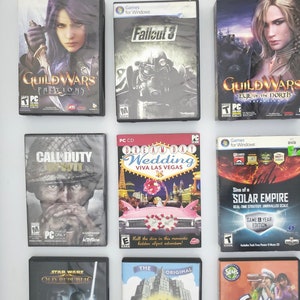 May include: A collection of video game cases, including Guild Wars, Fallout 3, Call of Duty, Dream Day Wedding, Sins of a Solar Empire, Star Wars: The Old Republic, Monopoly, and The Sims 2: Open for Business. The cases are arranged in two rows of four.