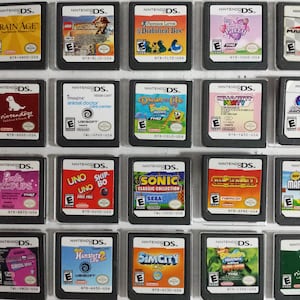 May include: A collection of 20 Nintendo DS game cartridges, including titles like Brain Age, Mario Kart DS, Hello Kitty Party, and Sonic Classic Collection. The cartridges are arranged in a grid pattern on a black surface.