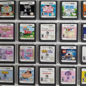 May include: A collection of 18 Nintendo DS game cartridges, displayed in a binder. The cartridges are arranged in three rows of six. The cartridges are all different colors and have different titles, including "Tangled", "Dora", "Big Brain Academy", "Ice Age", "Imagine Fashion Designer", "Hello Kitty Party", "Team Umizoomi", "Disney Princess", "Dora Saves the Mermaids", "Petz Catz Clan", "Lego Harry Potter", "Imagine Babyz", "Catz", "Cooking Mama", "Imagine Zookeeper", "Pinkalicious", and "Plants vs. Zombies".