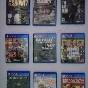 May include: A collection of nine PlayStation 4 video game cases. The cases are arranged in three rows of three. The games include The Show 17, Call of Duty: WWII, The Last of Us Remastered, The Crew 2, Call of Duty: Ghosts, Grand Theft Auto V, Injustice 2, LittleBigPlanet 3, and Flashback Classics vol. 2.