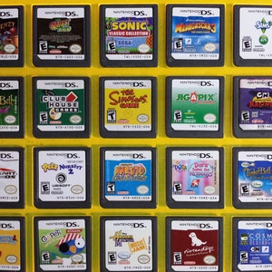 May include: A collection of 18 Nintendo DS game cartridges displayed in a yellow plastic case. The cartridges are arranged in three rows of six. The cartridges are all different colors and have different game titles on them.