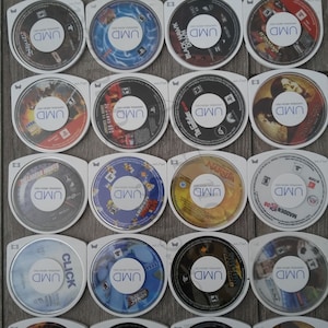 Puede incluir: Una colección de 18 discos UMD blancos para la consola de videojuegos Sony PlayStation Portable (PSP). Los discos están dispuestos en una cuadrícula y presentan una variedad de títulos de juegos, que incluyen Madden 08, Black Hawk Down y Sonic Unleashed.
