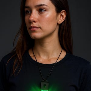 May include: A black t-shirt with the word "ILLENIUM" in bright green neon lettering. A matching green neon pendant hangs from a black cord necklace. The image is a medium shot of a person.