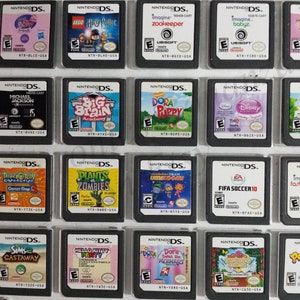 May include: A collection of 18 Nintendo DS game cartridges, displayed in a clear plastic case. The cartridges feature a variety of popular titles, including "Tangled", "Dora the Explorer", "Plants vs. Zombies", and "FIFA Soccer 10".
