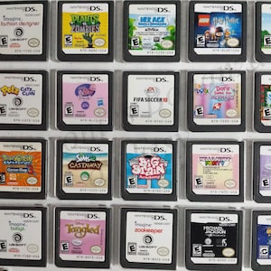 May include: A collection of 20 Nintendo DS game cartridges, displayed in a plastic case. The cartridges are arranged in four rows of five. The games include titles such as Plants vs. Zombies, Dora the Explorer, and Tangled.
