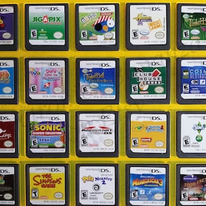 May include: A collection of 18 Nintendo DS game cartridges displayed in a yellow plastic case. The cartridges are arranged in three rows of six. The cartridges are all different colors and have different game titles on them. Some of the titles include "CN Racing", "Jigapix", "Go Pets", "Tinker Bell", "Naruto", "Dora", "Nintendogs", "Sonic", "Mario Kart", "Crayola", "The Simpsons Game", "Petz Nursery", "Madagascar", and "Food Frenzy".