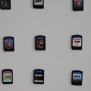 Puede incluir: Una colección de cartuchos de juegos de PS Vita, cada uno con arte de portada y títulos únicos. Los juegos incluyen "Killzone", "Call of Duty", "MLB The Show" y "Michael Jackson". Los cartuchos se muestran sobre un fondo blanco.