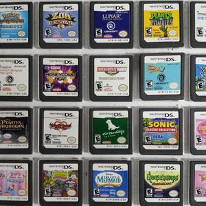 May include: A collection of 18 Nintendo DS game cartridges displayed in a clear plastic case. The cartridges are arranged in three rows of six. The cartridges are all different colors and have different game titles on them.