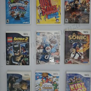 May include: A collection of nine video game cartridges for the Nintendo Wii console. The games include Skylanders Trap Team, Just Dance Kids 2, LEGO Lord of the Rings, LEGO Batman 2 DC Super Heroes, Madden NFL 13, Sonic and the Secret Rings, Monster Hunter 3, Club Penguin Game Day, and Kidz Bop.