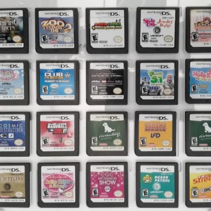 May include: A collection of 16 Nintendo DS game cartridges displayed in a clear plastic case. The cartridges are arranged in four rows of four, with each cartridge featuring a different game title and cover art. Some of the games include "Vampire Secrets", "Zoo Tycoon DS", "Club Penguin", "Cosmic Destruction", "Major League Baseball 2K7", "Nintendogs", "The Settlers", "Hello Kitty & Friends", "Egg My Fashion Show", "Ocean Patrol", and "Street 2".