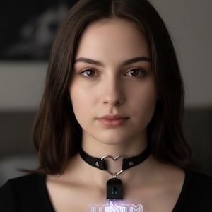 May include: Black leather choker with a silver heart-shaped pendant. A rectangular pendant with the word "ILLENIUM" in white lettering is suspended from the heart. The pendant has a blue neon glow.