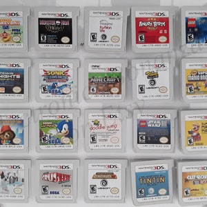 May include: A collection of 18 Nintendo 3DS game cartridges, displayed in a grid on a white surface. The cartridges are in various colors and feature different game titles, including "Super Monkey Ball 3D", "Monster High 13 Wishes", "Imagine Fashion Life", "Angry Birds Trilogy", "Lego Harry Potter", "Tenka Knights", "Sonic All-Stars Racing Transformed", "Minecraft", "Rayman Origins", "Super Mario Bros. 2", "Paper Mario", "Sonic Lost World", "Doodle Jump", "Lego Star Wars III", "Super Mario Maker 3DS", "Animal Crossing: New Leaf", "Crushed", "Rayman Legends", "The Adventures of Tintin", and "Cut the Rope 2".