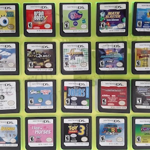 May include: A collection of 16 Nintendo DS game cartridges displayed in a clear plastic case. The cartridges are arranged in a 4x4 grid and feature a variety of popular games, including "Brain Boost", "Math Blaster", "Up", "ATV Quad Frenzy", "Hannah Montana", "Imagine Fashion Designer", "The Sims 2: Apartment Pets", "Jonas", "Lego Batman", "I Love Horses", "Toy Story 3", "Super Mario", "iCarly 2", and "Downhill Domination 2008".