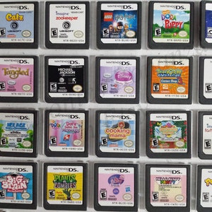 May include: A collection of 18 Nintendo DS game cartridges, displayed in a black plastic case. The cartridges feature a variety of popular children's games, including Dora the Explorer, Hello Kitty, and Plants vs. Zombies.
