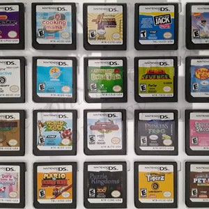 Op de afbeelding: Een verzameling van 15 Nintendo DS-spelcartridges die in een doorzichtige plastic doos worden getoond. De cartridges zijn gerangschikt in drie rijen van vijf. De cartridges zijn allemaal in verschillende kleuren en hebben verschillende speltitels. Sommige van de titels zijn "Cooking Mama", "World Zoo", "Princess Frog", "Tigerz" en "Pet Vet".