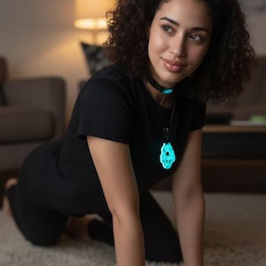 May include: Black t-shirt and leggings with a matching choker and pendant. The pendant and choker glow with a turquoise light. The person is kneeling on a light-colored carpet.