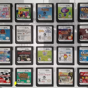 May include: A collection of 18 Nintendo DS game cartridges, displayed in a clear plastic case. The cartridges are arranged in three rows of six, with each cartridge featuring a different game title and cover art. Some of the games include "Dora the Explorer", "Animal Crossing", "Metroid Prime Hunters", "Lego Indiana Jones", and "Club Penguin".